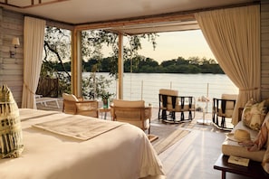 Un dormitorio con una cama grande, dos sillones, una mesita y vista a un cuerpo de agua.
