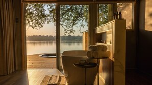 A spa room with a large bathtub, wooden flooring, and a view of a lake.