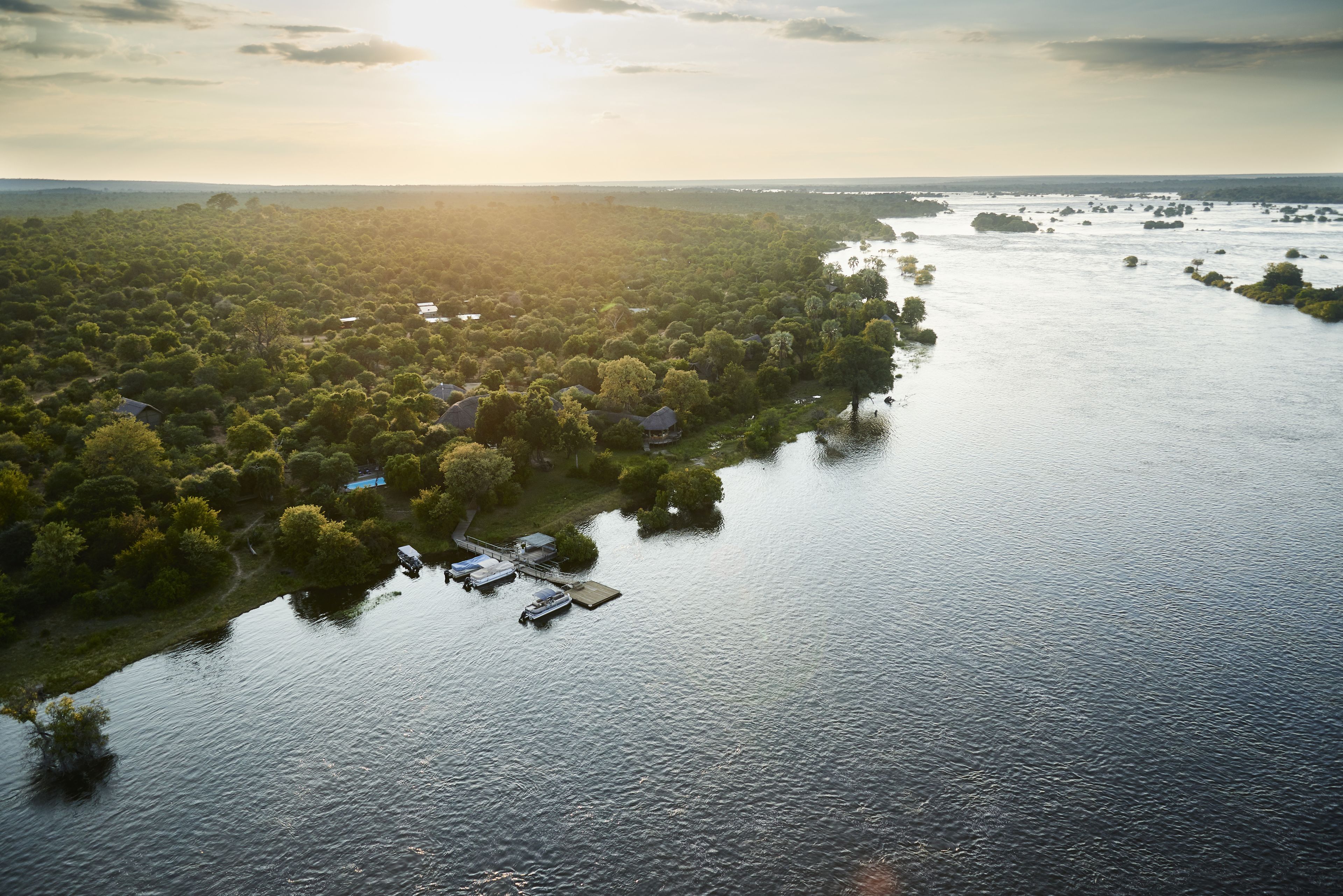 Vue aérienne d’une propriété au bord du lac, avec un quai, des bateaux et la végétation environnante.