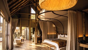 A bedroom with a large bed, a wooden bench, a bathtub, and a desk with a lamp.
