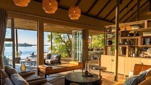 A spacious living area with a view of a lake, furnished with sofas, a coffee table, and a bookshelf.