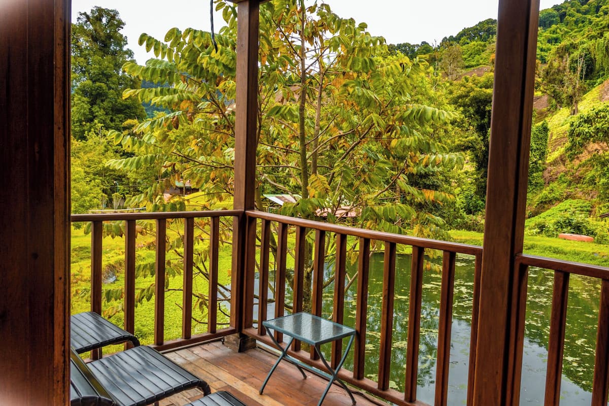 A wooden deck with two chairs and a table overlooking a river surrounded by lush greenery and hills.