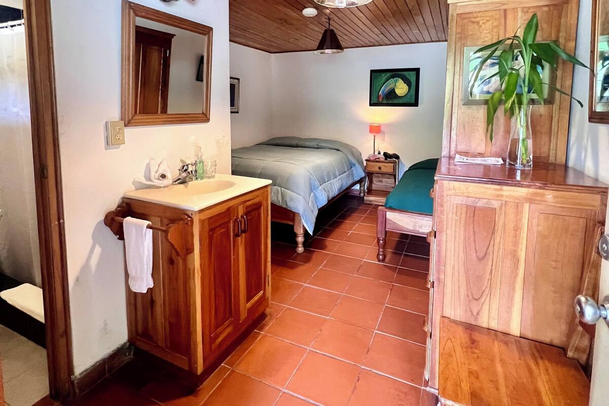 A bedroom with a wooden ceiling, a bed, a nightstand, a mirror, a sink, and a cabinet.