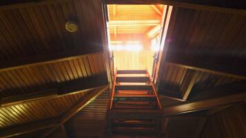 Een houten trap leidt naar een heldere, warm verlichte kamer met een houten plafond en wanden.