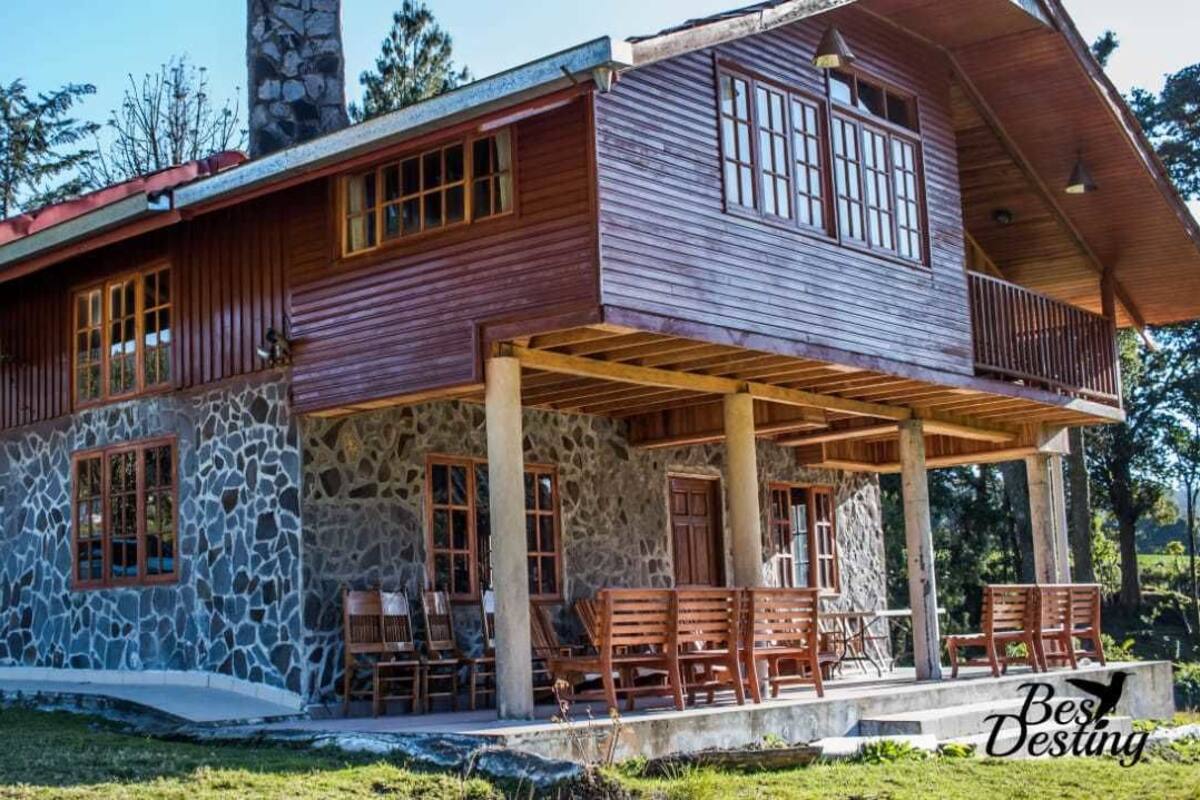 A two-story stone house with a wooden exterior, a balcony, and outdoor seating.