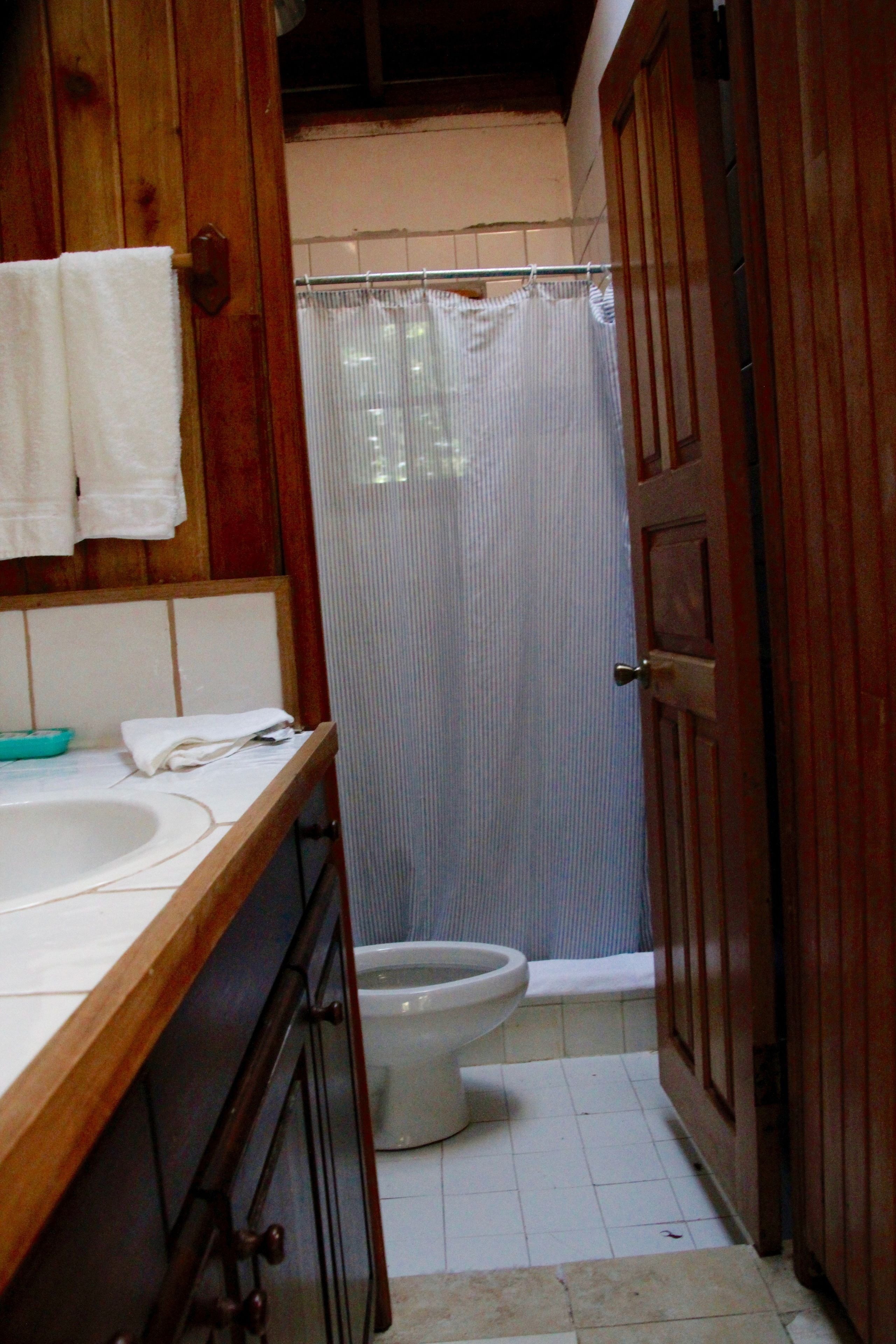 A bathroom with a wooden vanity, a white sink, a toilet, and a shower curtain.