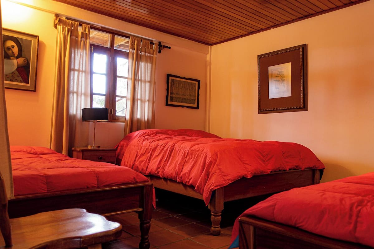 A bedroom with two single beds, a wooden headboard, a nightstand with a lamp, and a window with curtains.