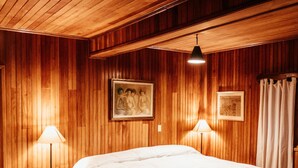 A wooden-paneled bedroom with a large bed, two bedside lamps, and framed artwork on the walls. - Los Quetzales Ecolodge & Spa (Cerro Punta)