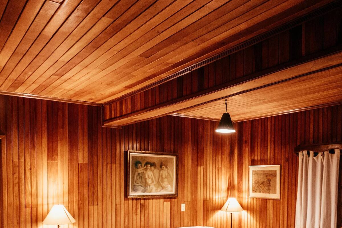 A wooden-paneled bedroom with a large bed, two bedside lamps, and framed artwork on the walls.