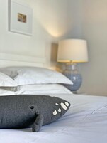 Una cama con un almohadón y un peluche de ballena, ambos grises.