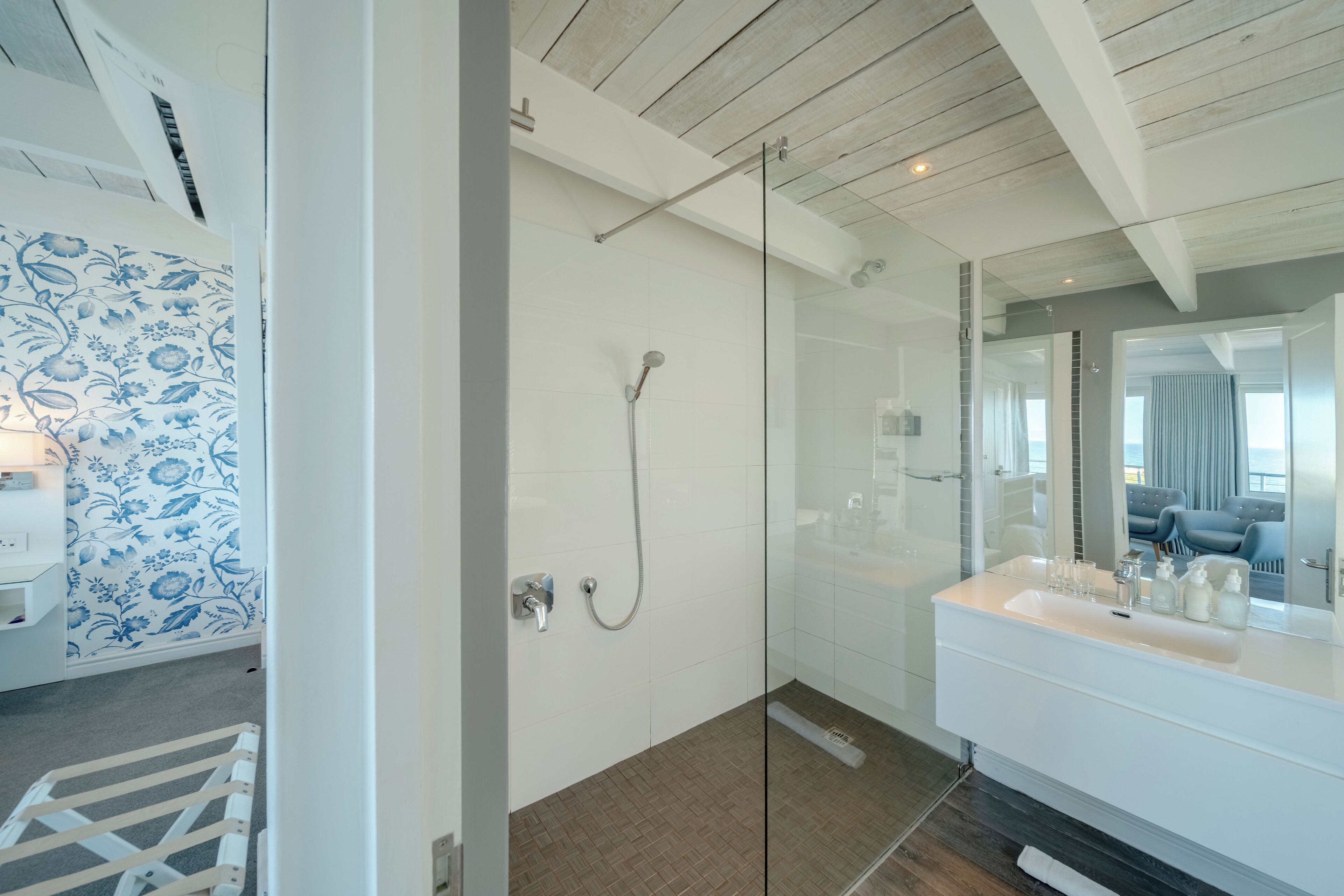 A modern bathroom with a glass shower enclosure, a white sink with toiletries, and a patterned wall.