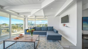 A modern living room with a blue sofa, a wooden coffee table, and a large window offering a city view.