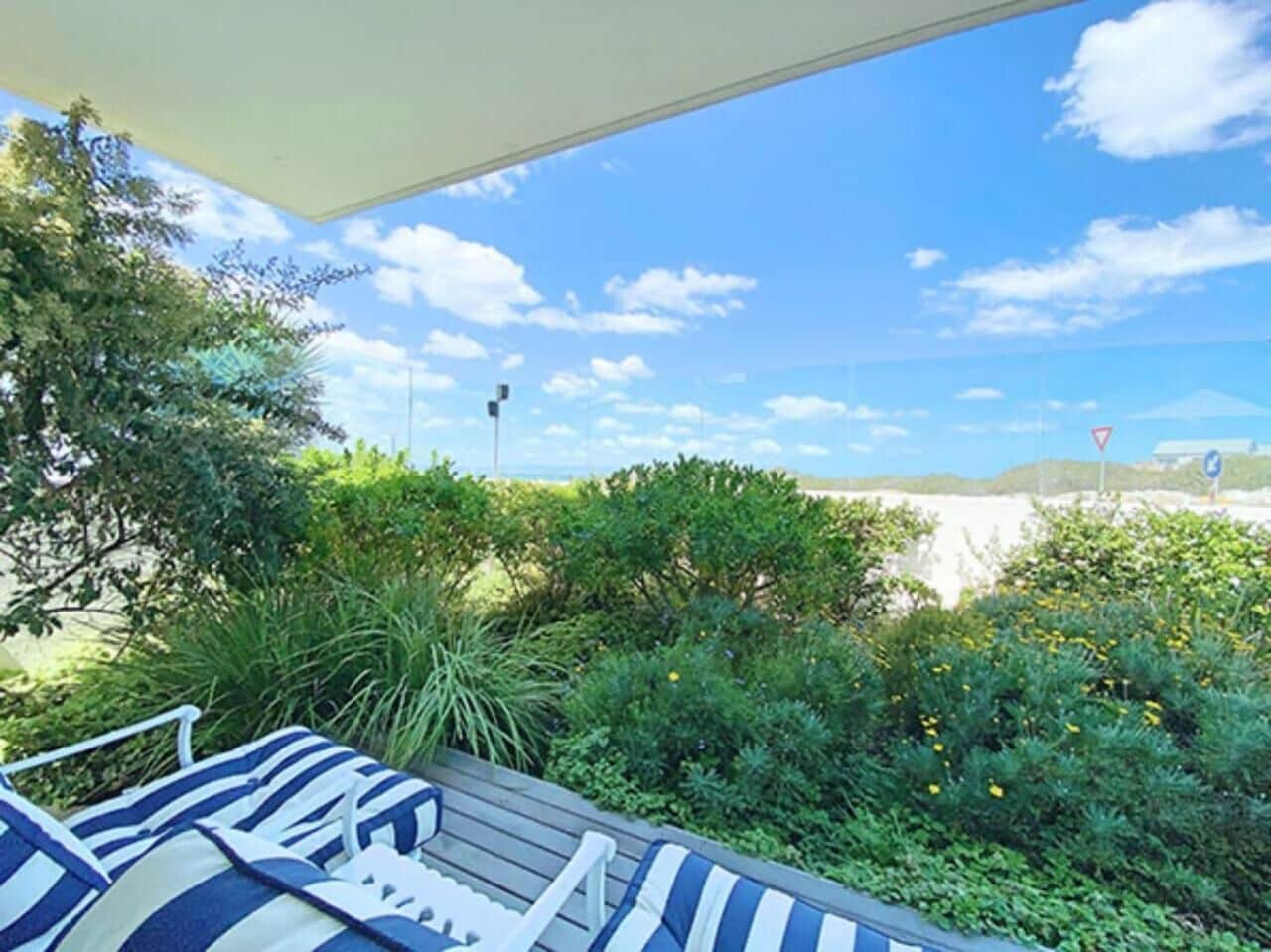 Un espacio al aire libre cubierto con piso de madera, cojines a rayas y vista a la playa y al cielo.