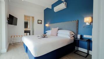Una habitación de hotel moderna con una cama grande, un televisor de pantalla plana, una mesita de noche con lámpara y un equipo de aire acondicionado.