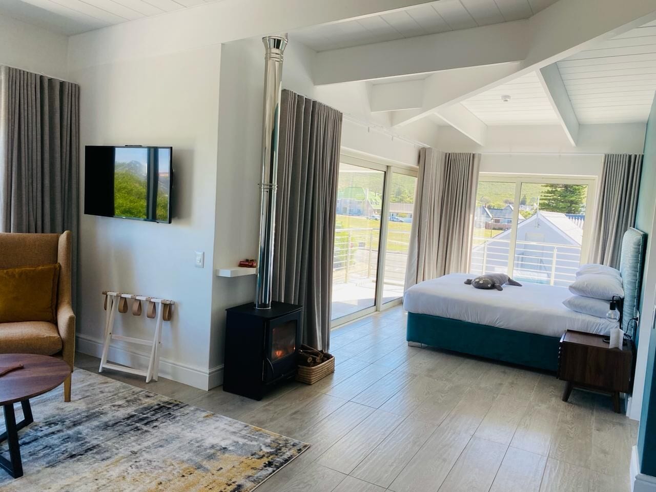 A modern bedroom with a large bed, a fireplace, a TV, and a view of the outdoors.