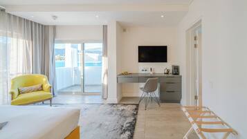 A modern hotel room with a bed, a desk, a chair, a TV, and a view of the sea.