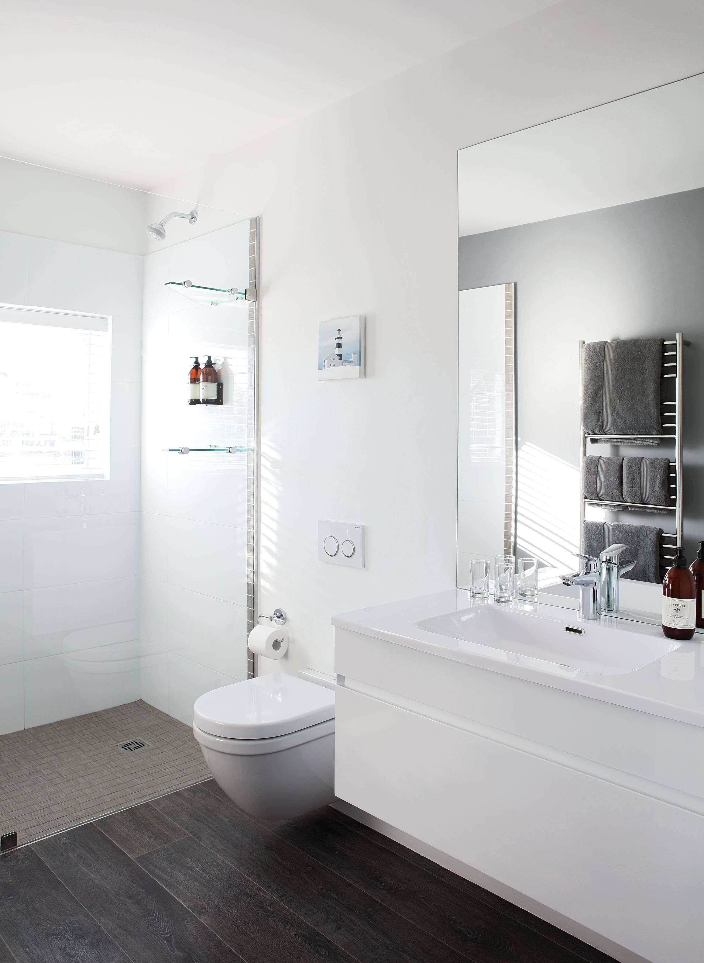 A modern bathroom with a toilet, sink, and shower. There is a towel rack with towels and a mirror above the sink.