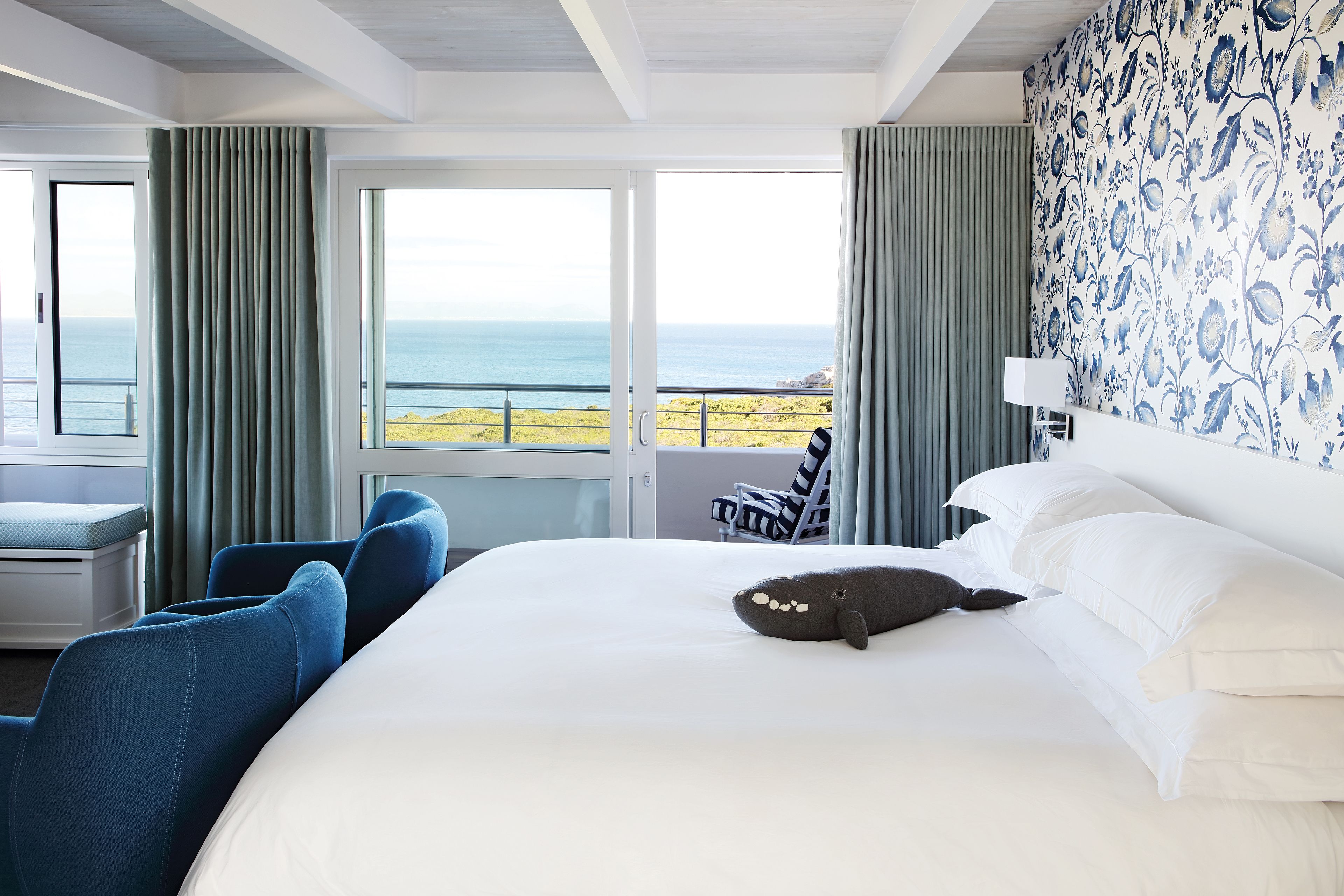 A hotel room with a large bed, a view of the sea, and a balcony with a chair.