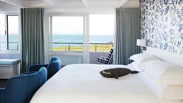 A hotel room with a large bed, a view of the sea, and a balcony with a chair.