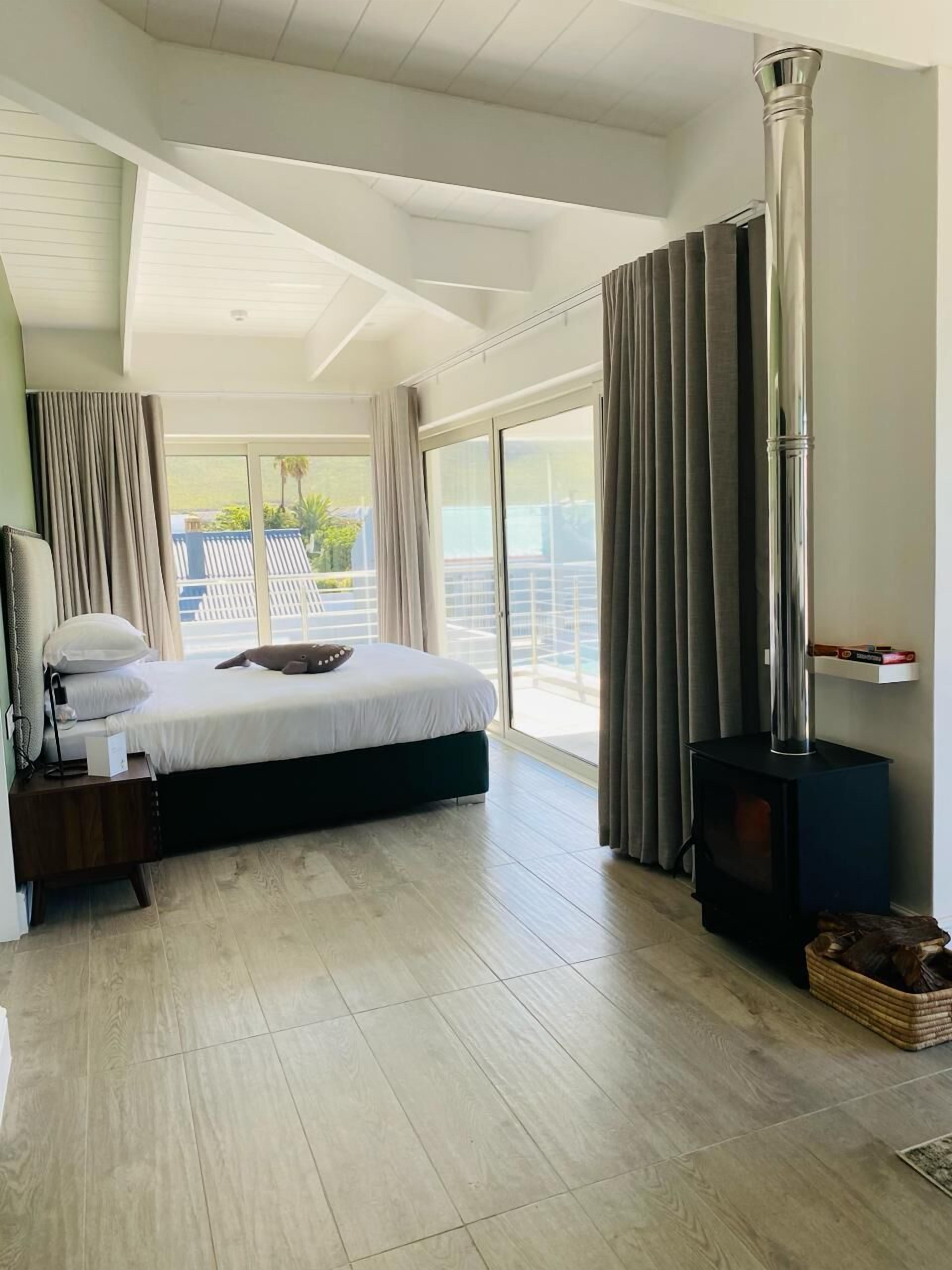 A modern bedroom with a large bed, a wooden floor, a fireplace, and a balcony with curtains.