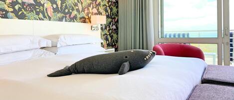 A hotel room with a large bed, a view of the sea through a window, and a tropical floral wallpaper.