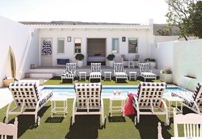 Zona junto a la piscina con sillones de descanso, una mesita y una cama al fondo.