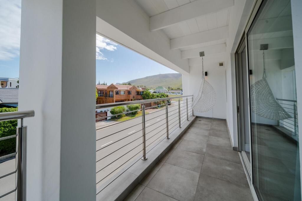 Un balcon doté d’une rambarde en métal, d’une porte vitrée et offrant une vue sur des maisons et des montagnes en arrière-plan.