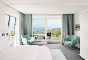 Habitación de hotel con una cama grande, dos sillones, un balcón con vistas al mar y un armario blanco.