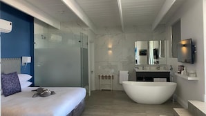 A modern hotel room with a large bed, a bathtub, a glass shower enclosure, and a mounted TV.