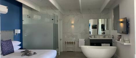 A modern hotel room with a large bed, a bathtub, a glass shower enclosure, and a mounted TV.