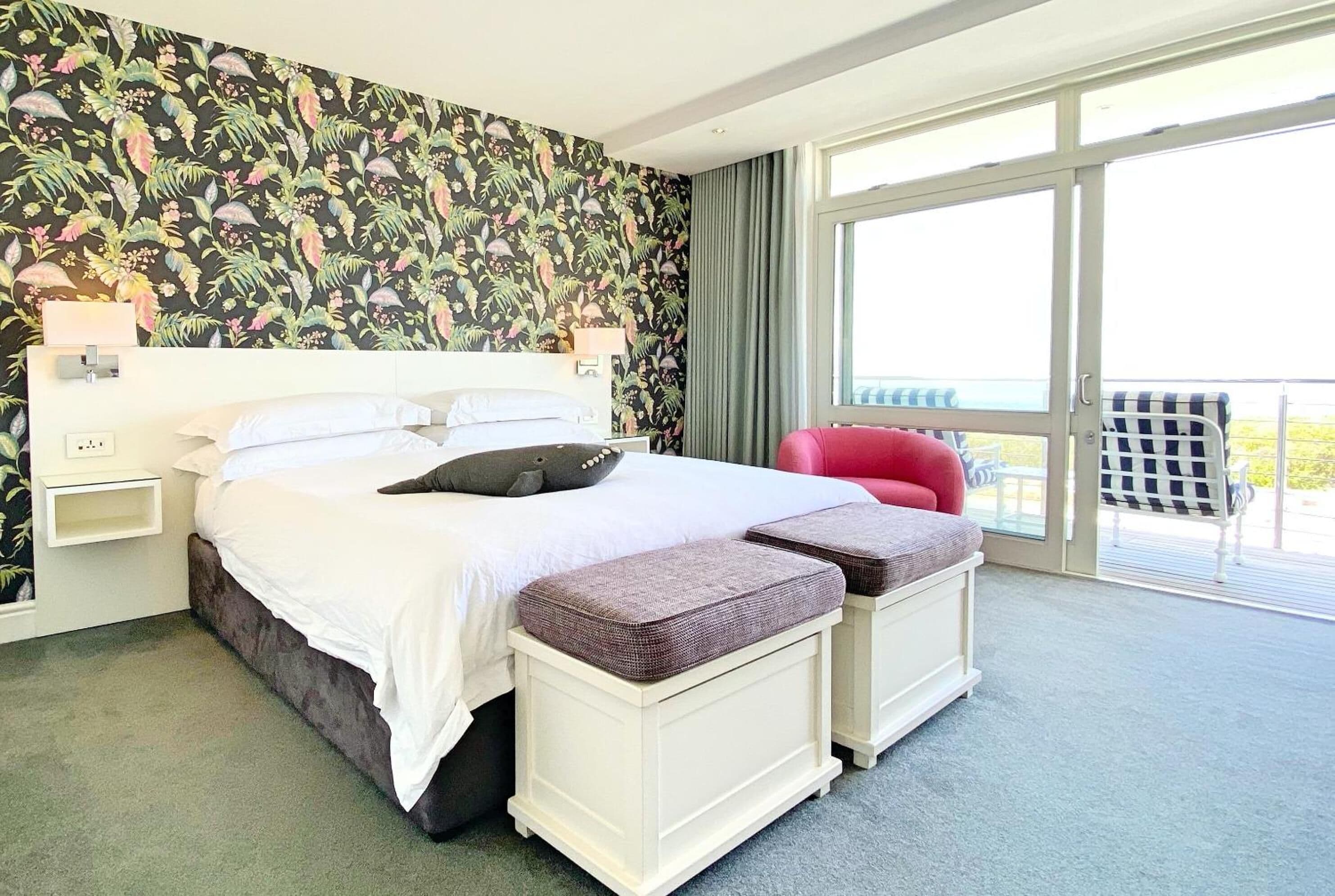 Una habitación de hotel con una cama grande, un balcón con una silla roja y un papel tapiz floral.