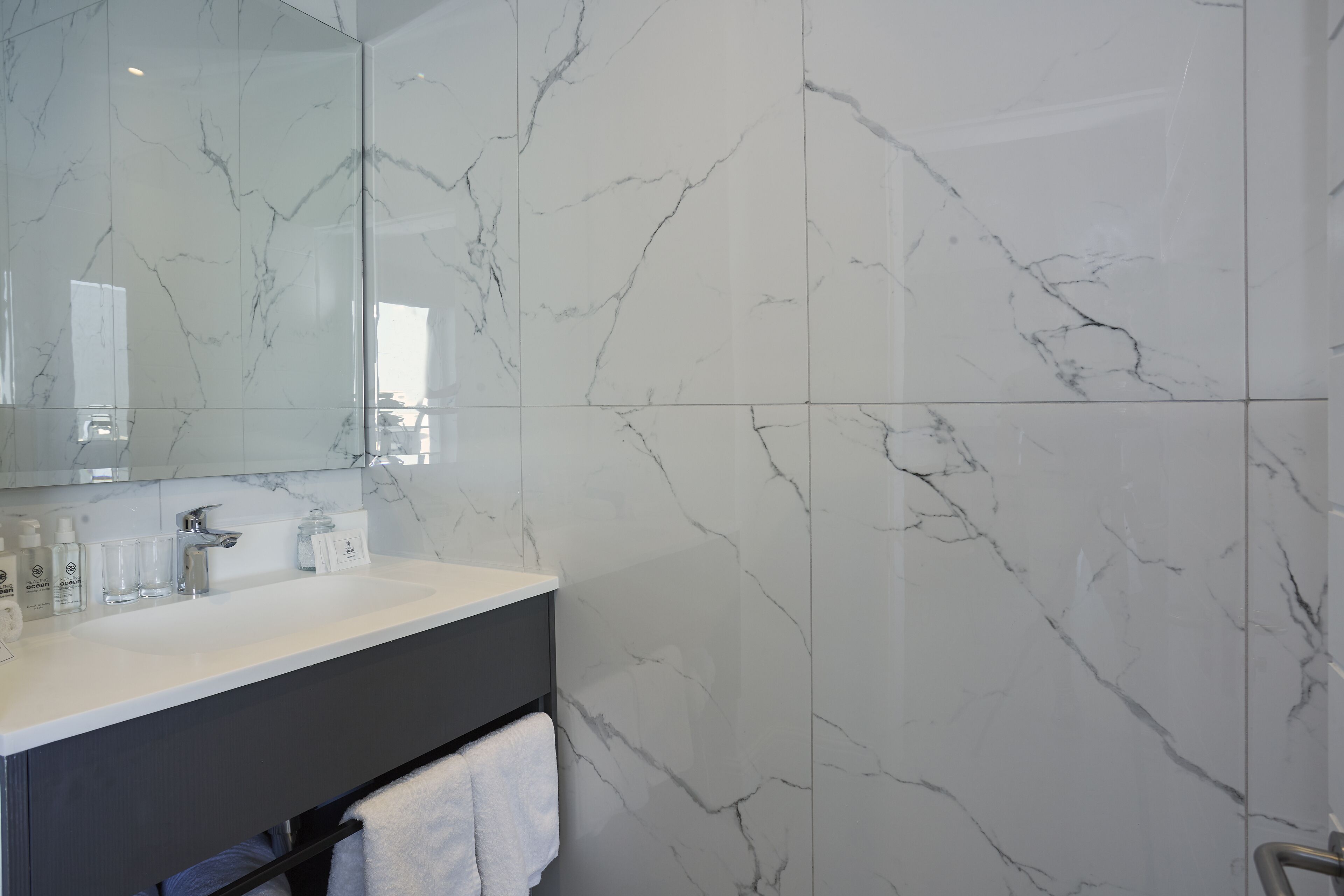 A modern bathroom with a marble backsplash, a white sink, and a large mirror.