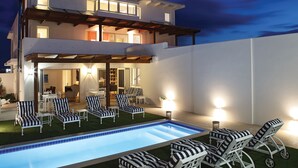 A modern two-story house with a swimming pool, outdoor seating, and a well-lit patio area.