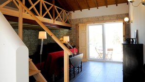 A spacious room with a wooden staircase, stone walls, and a large sliding glass door leading to an outdoor area. - Casa das Rendufas (Torres Novas)