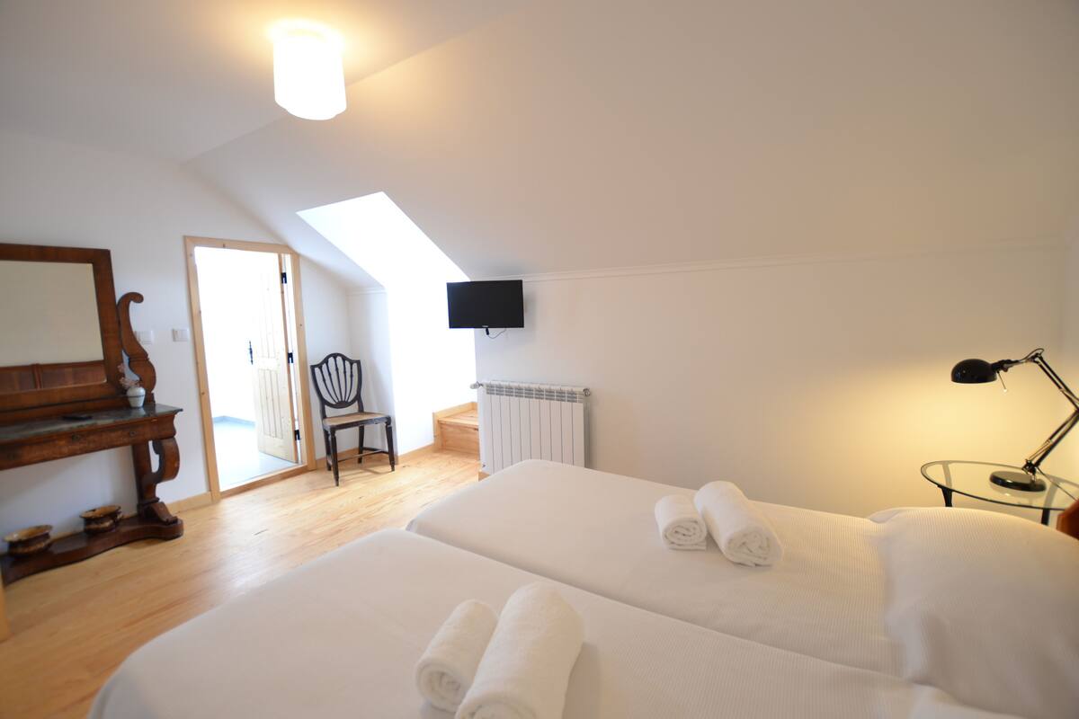 A bedroom with two beds, a TV mounted on the wall, a desk, and a chair.