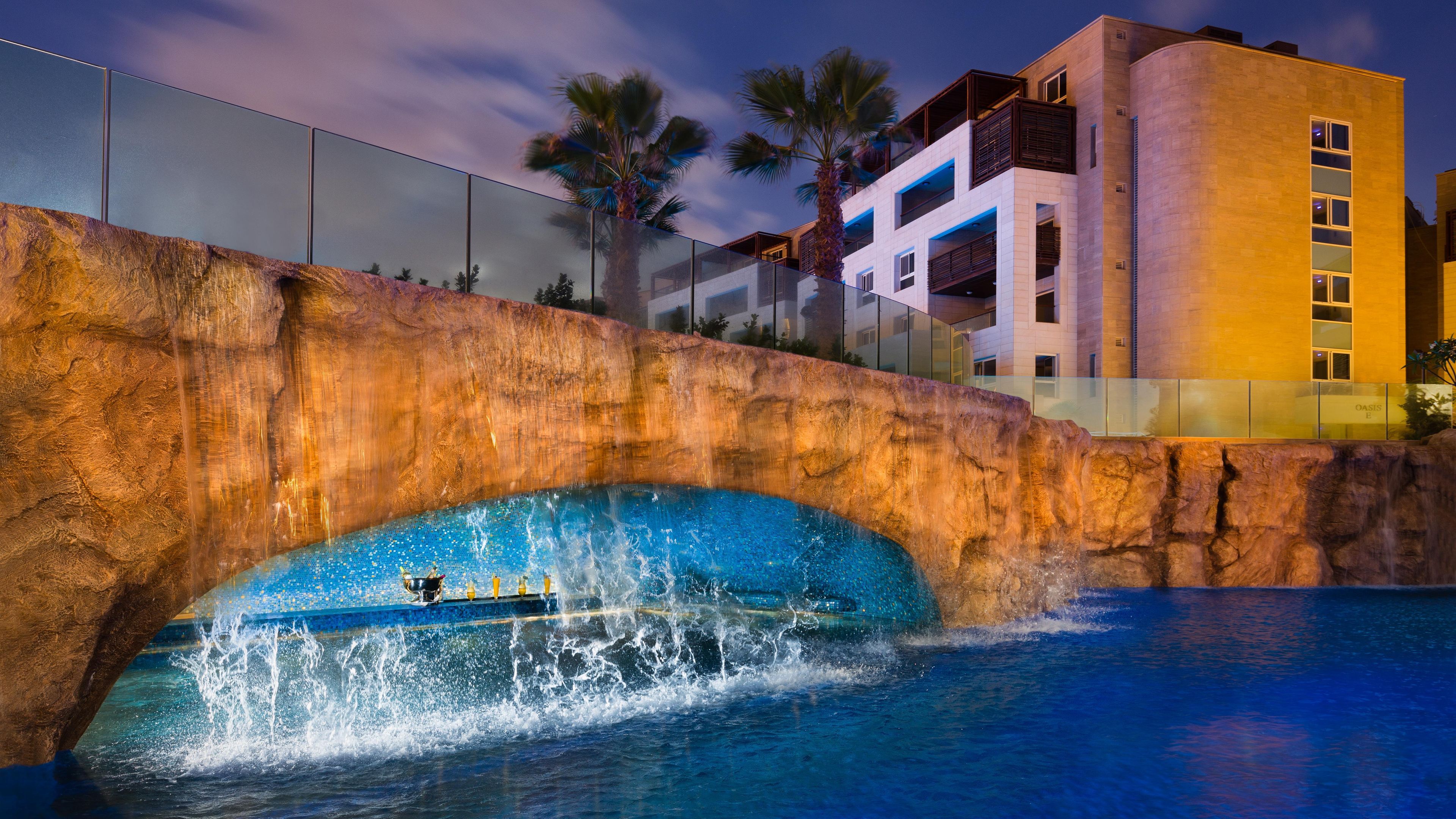 Une piscine agrémentée d’une cascade, un pont de pierre et un bâtiment doté de balcons.