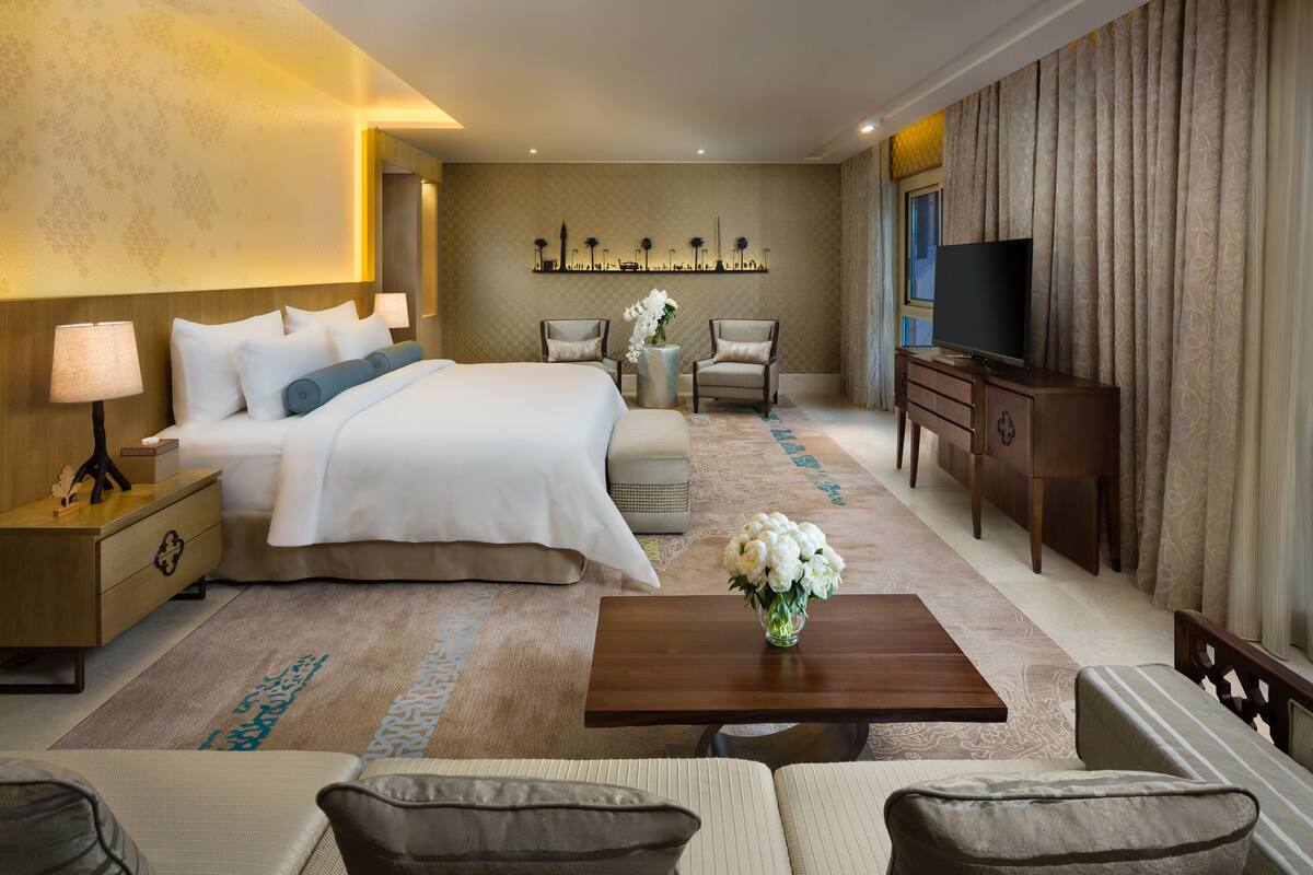 A hotel room with a large bed, a TV, a coffee table, a sofa, and a view of the city.