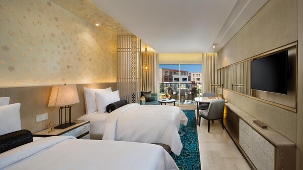 A hotel room with two beds, a TV, a desk, and a view of buildings. - Kempinski Summerland Hotel & Resort Beirut (Ghobeiry)