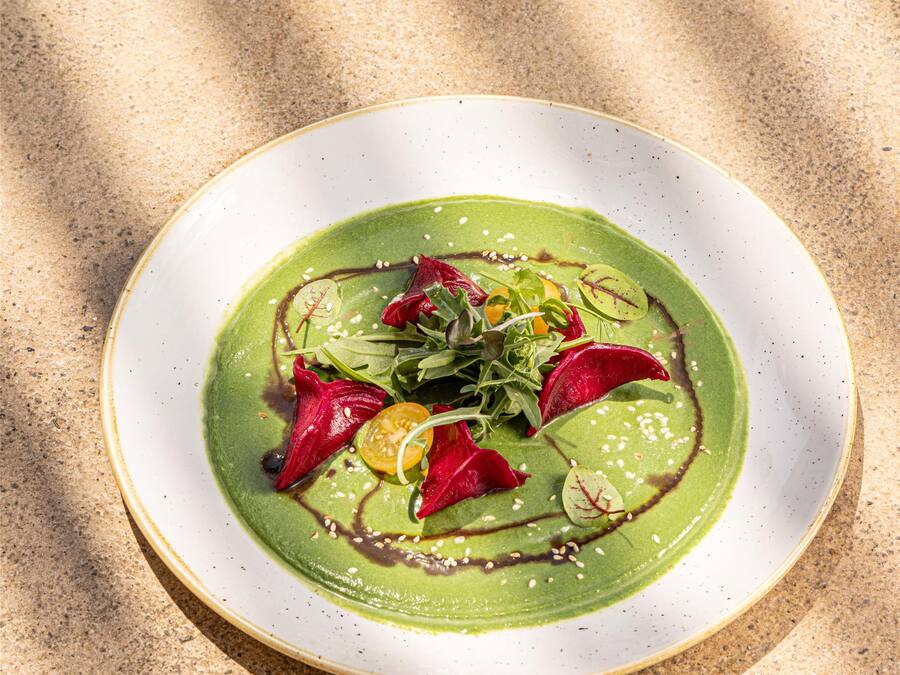 A plate of food with a green sauce, red and yellow vegetables, and sesame seeds on a white plate.