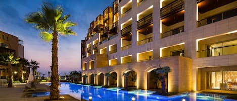Un hotel moderno con piscina, palmeras y balcones iluminados.