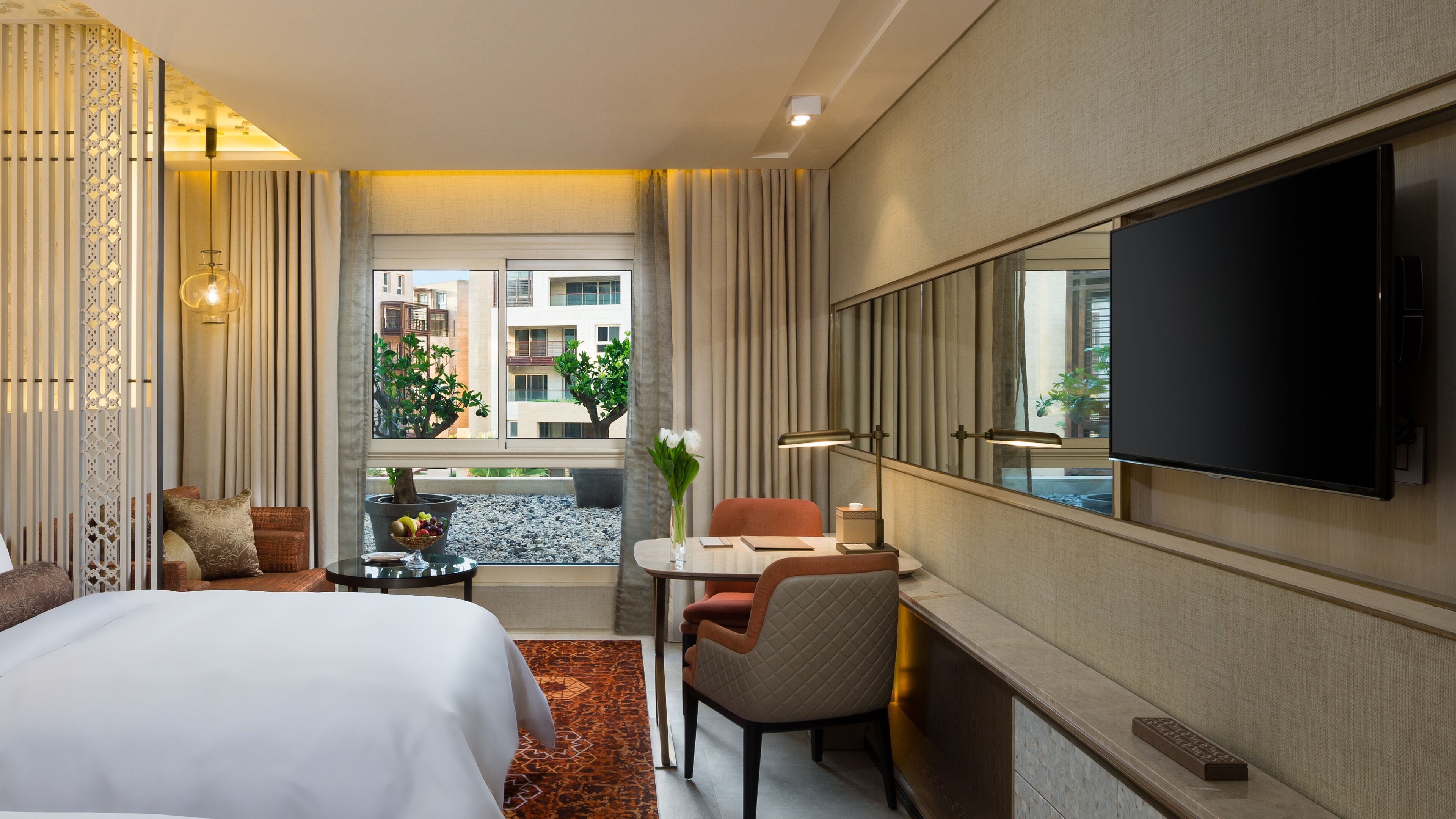 Habitación de hotel con cama, escritorio, silla, televisor y vistas a edificios exteriores.