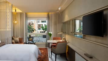 Habitación de hotel con cama, escritorio, silla, televisor y vistas a edificios exteriores.
