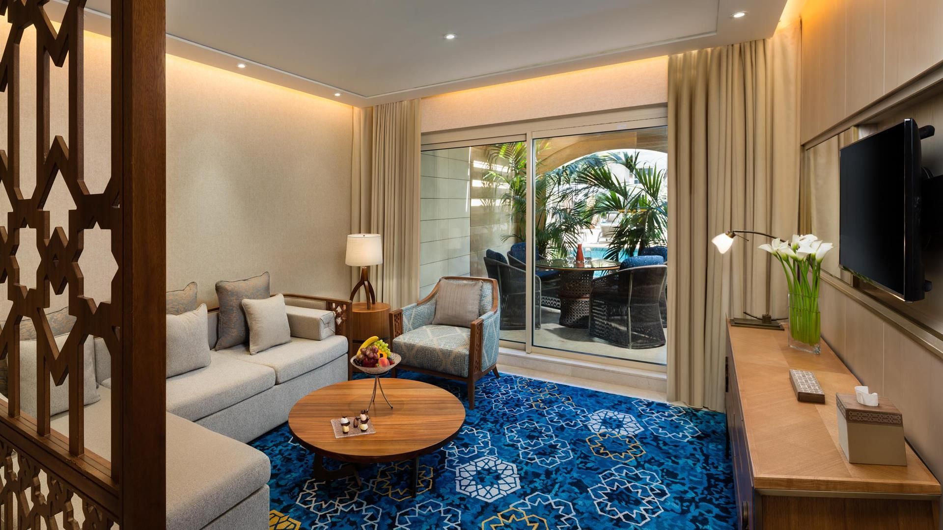 A hotel room with a sofa, armchair, coffee table, and a TV.