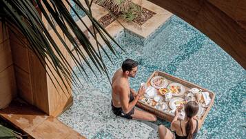 A couple dining by a pool with a mosaic tile floor and surrounding greenery.