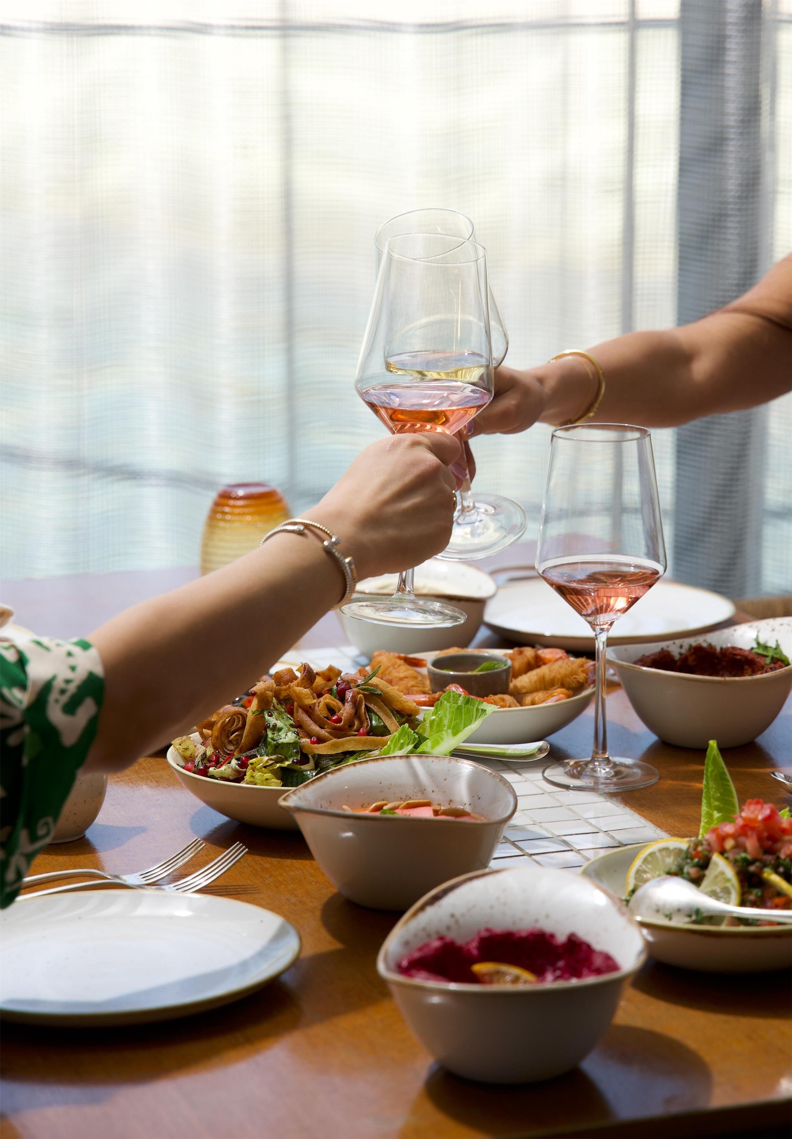 A dining table with various dishes, glasses of wine, and a window in the background.