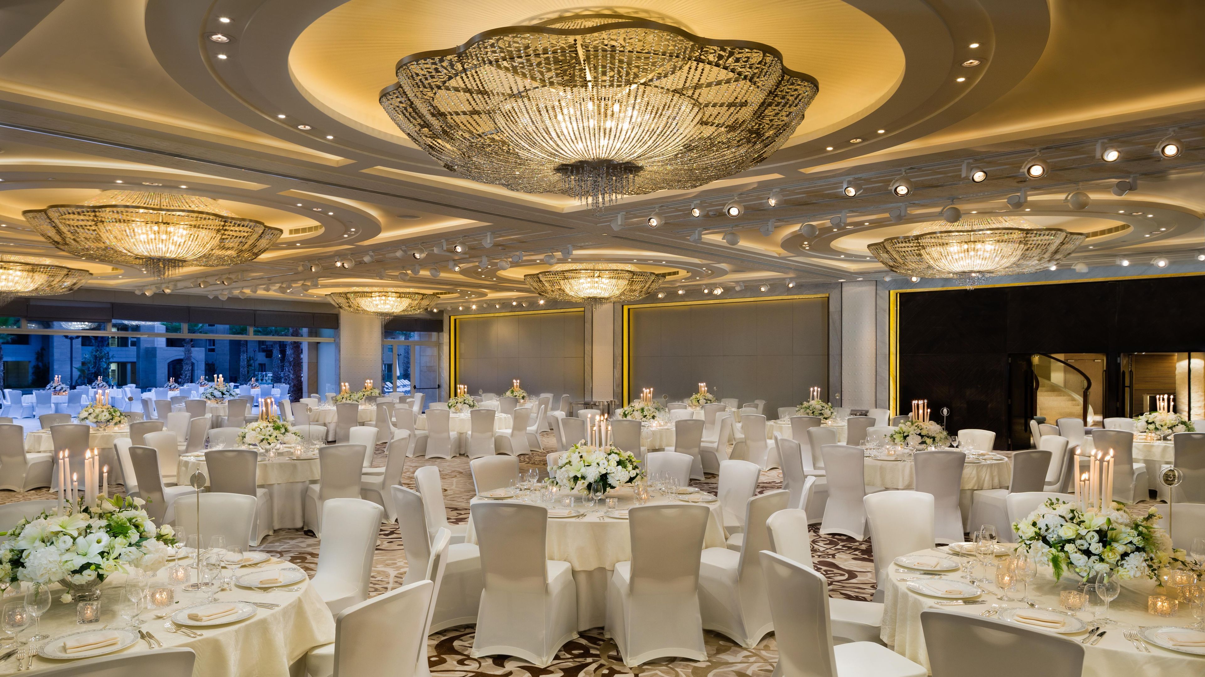 Une salle de banquet avec des tables rondes, des chaises blanches et des lustres.
