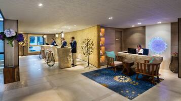 A hotel reception area with a reception desk, seating, and a decorative tree sculpture.