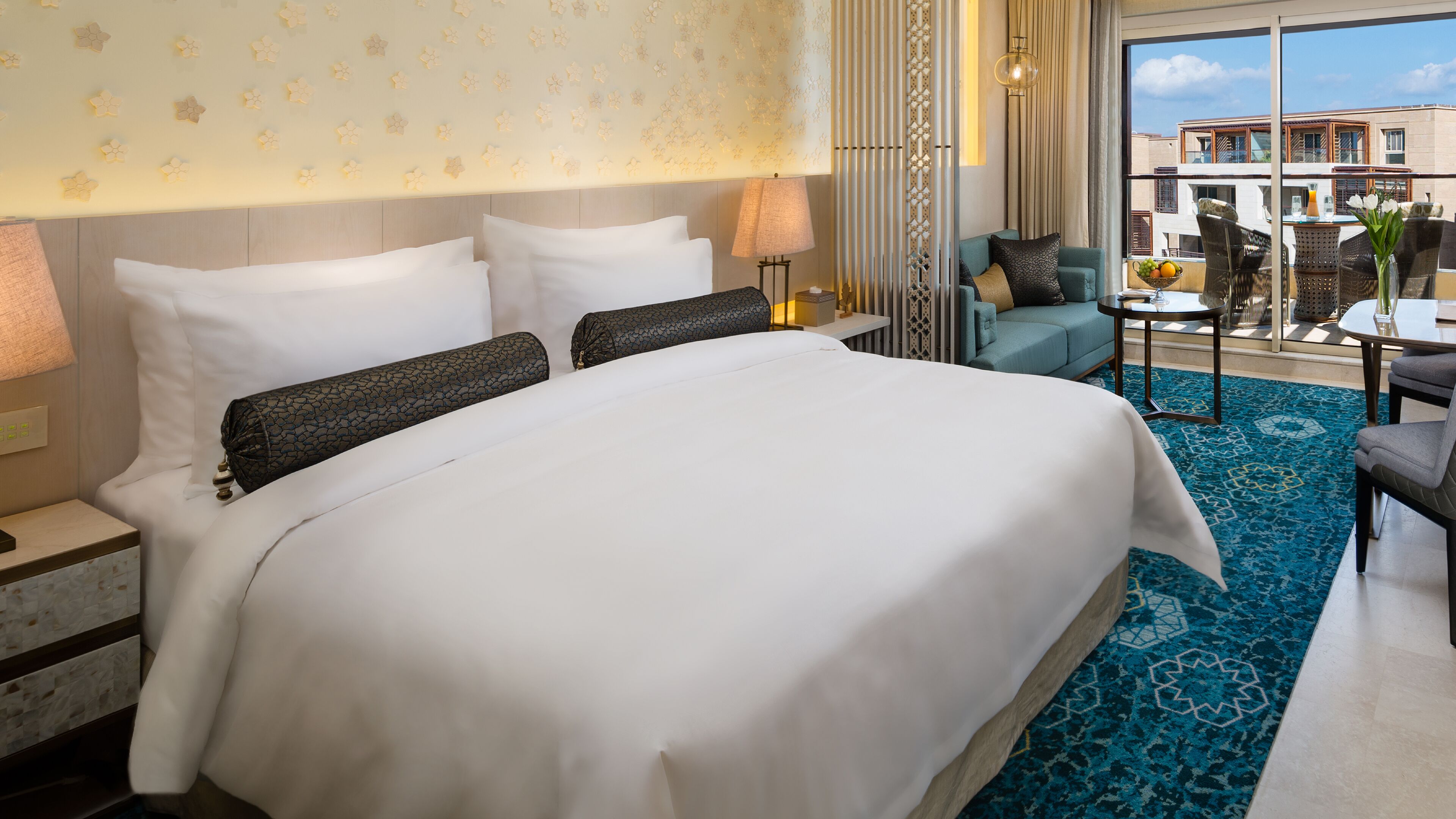 A hotel room with a large bed, a sitting area with a table and chairs, and a view of the city through large windows.