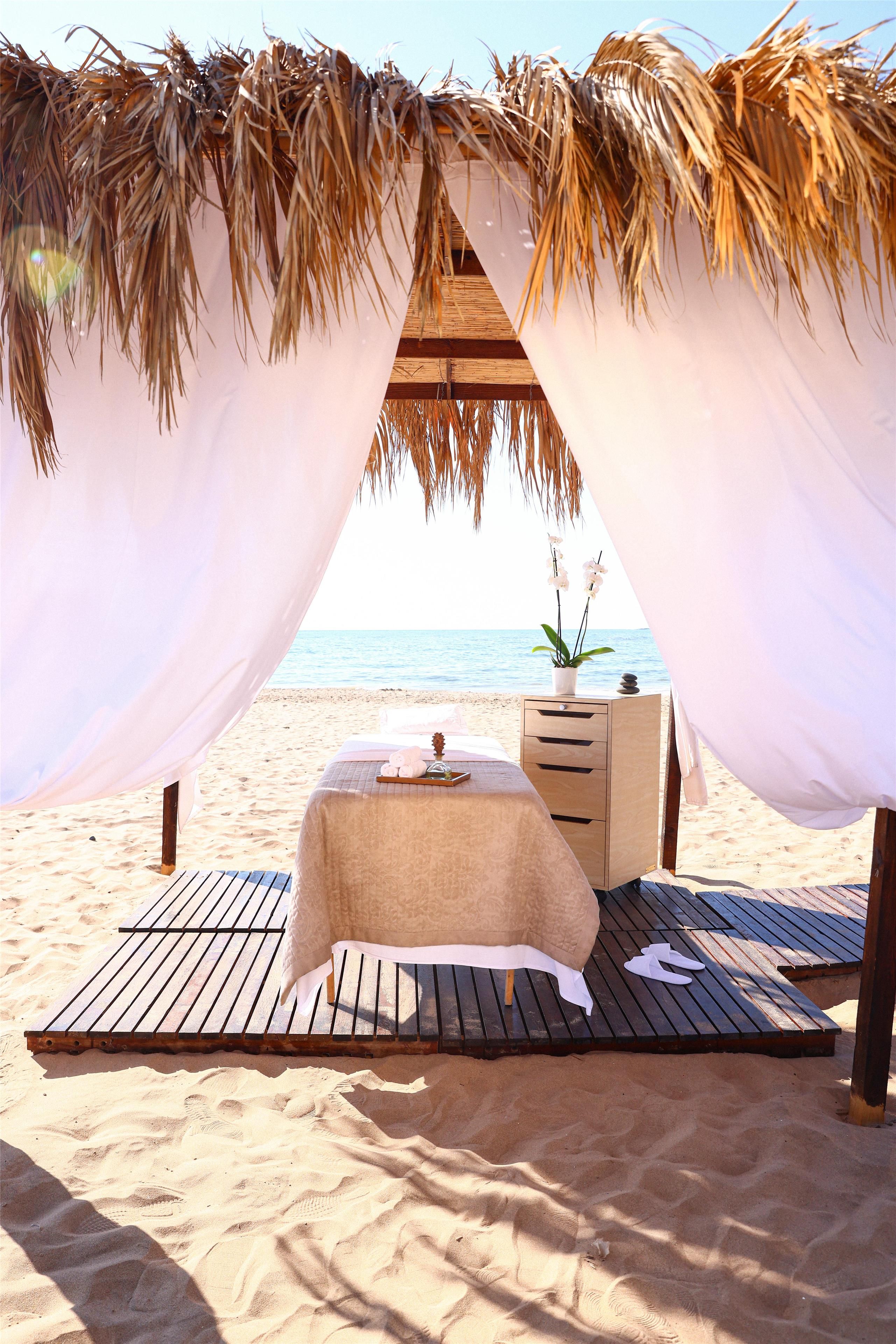 A beach setting with a canopy, a bed, a small table, and a nightstand.