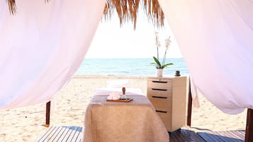 A beach setting with a canopy, a bed, a small table, and a nightstand.